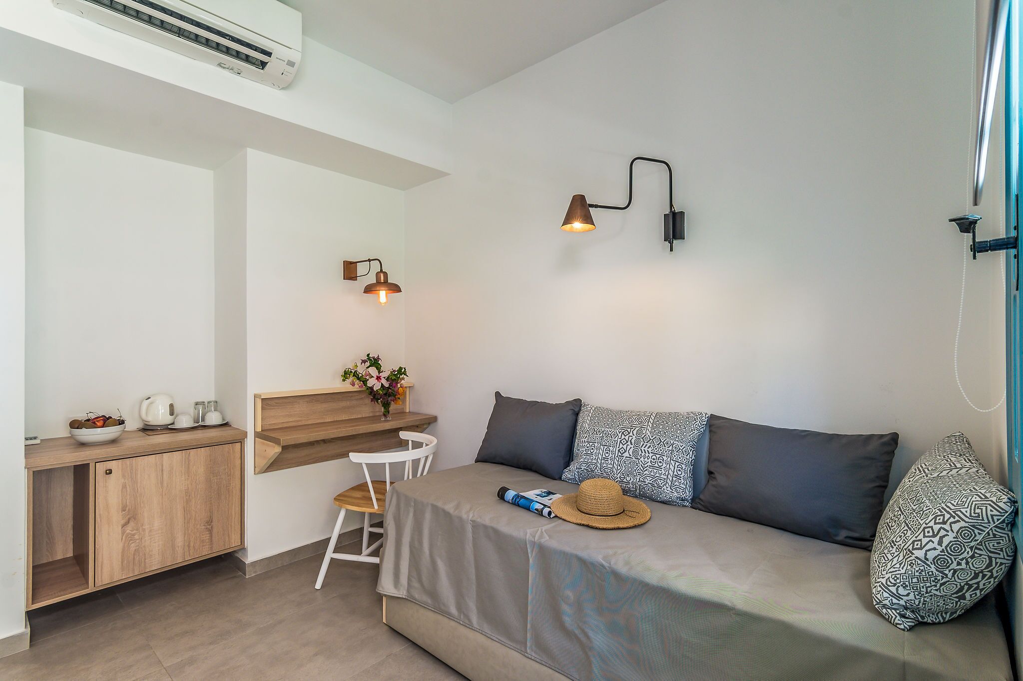 Une chambre moderne équipée d’un lit, d’un bureau et d’une chaise. On y trouve également un climatiseur fixé au mur et deux appliques murales.