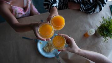 Drei Personen halten Gläser Orangensaft an einem Tisch mit einem Teller Essen und einer Saucenflasche.