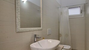 Une salle de bain avec un lavabo blanc, un miroir doté d’un cadre décoratif, un rideau de douche et une petite fenêtre.