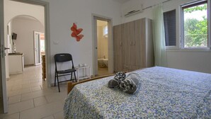 Une chambre à coucher comprenant un lit, une chaise, une armoire et une salle de bain visible à travers une porte ouverte.