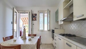 Una cocina compacta con estufa a gas, una mesa de comedor con sillas y vista a un espacio exterior por una puerta abierta.
