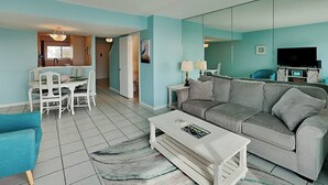 A living room with a sofa, coffee table, and a dining area with chairs and a table. - Tybee Lights 114C | Pet Friendly, Oceanfront! (Tybee Island)