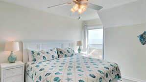 A bedroom with a bed, nightstands, a ceiling fan, and a view of the beach. - Tybee Lights 114C | Pet Friendly, Oceanfront! (Tybee Island)