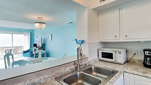 A modern kitchen with a stainless steel sink, white cabinets, and a microwave. - Tybee Lights 114C | Pet Friendly, Oceanfront! (Tybee Island)