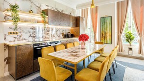Une cuisine moderne avec un revêtement mural en marbre, un îlot central et des chaises jaunes disposées autour d’une table en marbre.