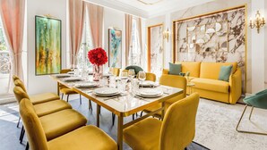 Un coin repas avec une longue table dressée pour six personnes, des chaises jaunes et un canapé jaune en arrière-plan.
