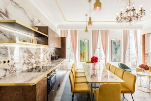 A modern kitchen with marble countertops, a central island, and a dining area with yellow chairs and a glass table. - Merveil - Luxury Suite - Marais - Antoine I (Paris)