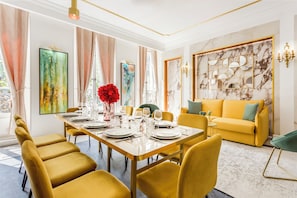A dining area with a long table set for six, yellow chairs, and a yellow sofa in the background.