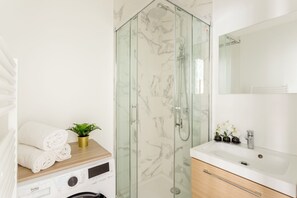 Un baño moderno con ducha de vidrio, lavamanos blanco y tocador de madera.