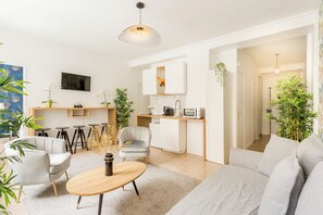 Un salon moderne comprenant un canapé, deux fauteuils, une table basse et un coin repas avec une petite table et des chaises. Il y a également un coin cuisine équipé d’un four à micro-ondes et de placards.