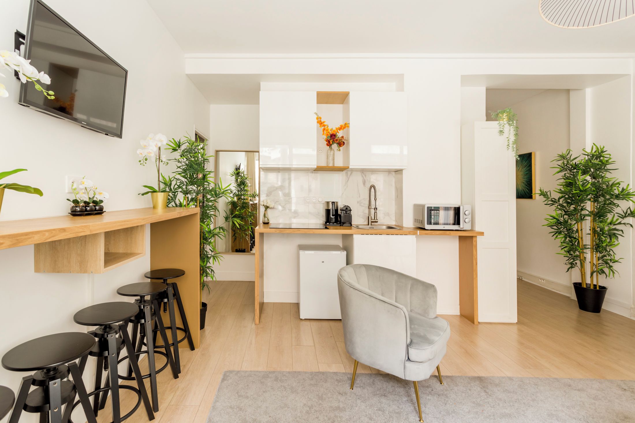 A modern kitchen with a built-in oven, microwave, and sink. There are bar stools and a grey chair.