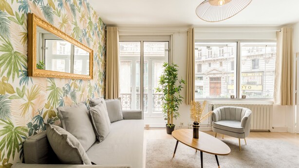 Een moderne woonkamer met een bank, fauteuil, salontafel, een grote spiegel en een plant in pot.