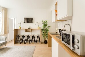 A modern kitchen with a microwave, bar stools, a potted plant, and a TV on the wall.