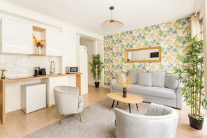 A modern living room with a sofa, a coffee table, and a kitchen area with a refrigerator and microwave.