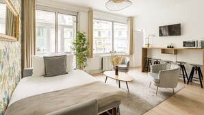 Een moderne hotelkamer met een groot bed, een klein tafeltje, een stoel, een televisie en uitzicht op de stad door grote ramen.