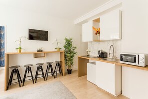 A modern kitchen with a white countertop, a microwave, a sink, and a potted plant.