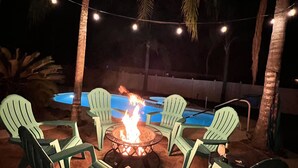 An outdoor seating area with chairs around a fire pit, a pool, and string lights in the background. - Relaxing Modern 3 br home with HEATED POOL (Palm Coast)