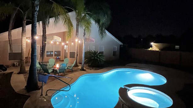 A swimming pool with a curved design, surrounded by palm trees and outdoor furniture. - Relaxing Modern 3 br home with HEATED POOL (Palm Coast)