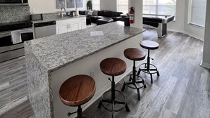 A spacious kitchen with a granite countertop, stainless steel appliances, and a bar area with stools. - Relaxing Modern 3 br home with HEATED POOL (Palm Coast)