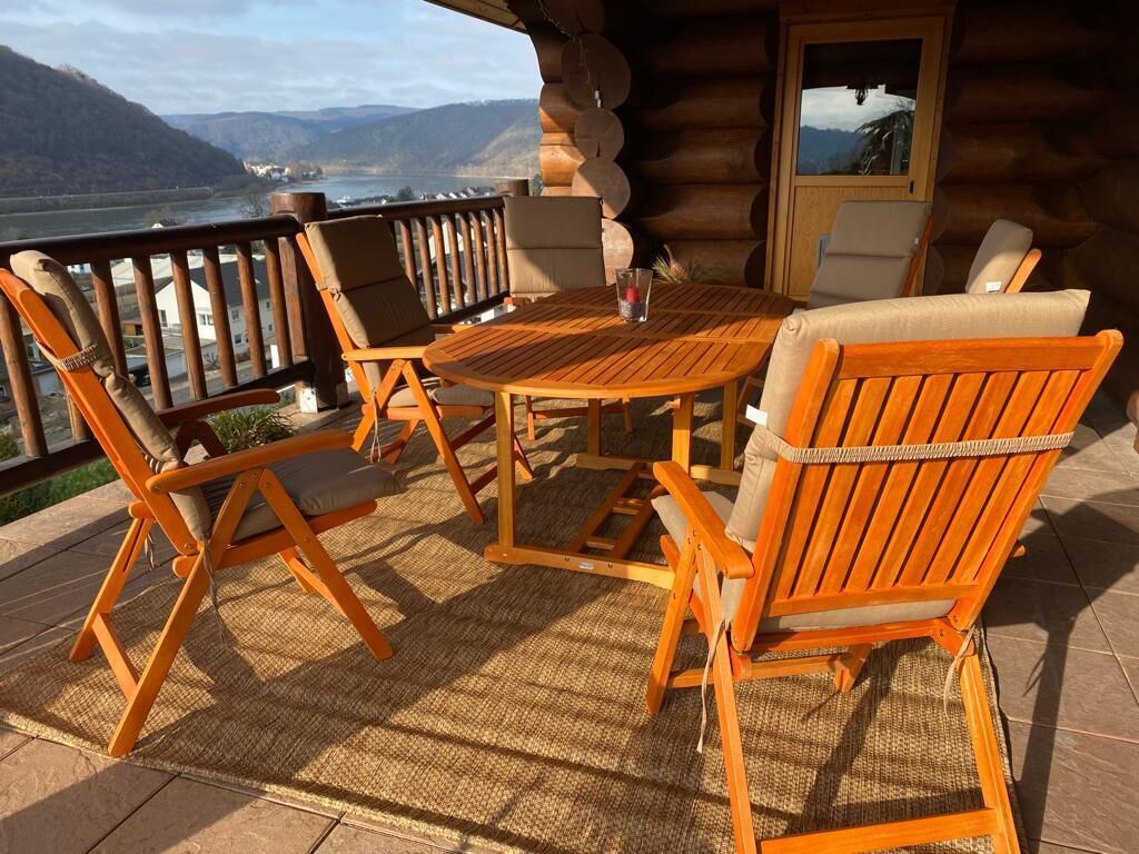 Ett trädäck med ett runt bord och fyra orangefärgade stolar, med utsikt över en flod och berg.