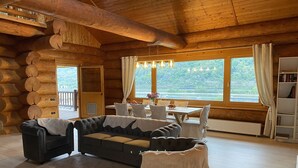 Ein Blockhaus-Interieur mit einer Sofagarnitur, einem Esstisch und großen Fenstern mit Blick auf einen See.