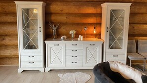 Ein Holzblockhaus-Interieur mit zwei weißen Schränken mit Glastüren, einem kleinen Tisch mit Dekoration und einem grauen Sofa.