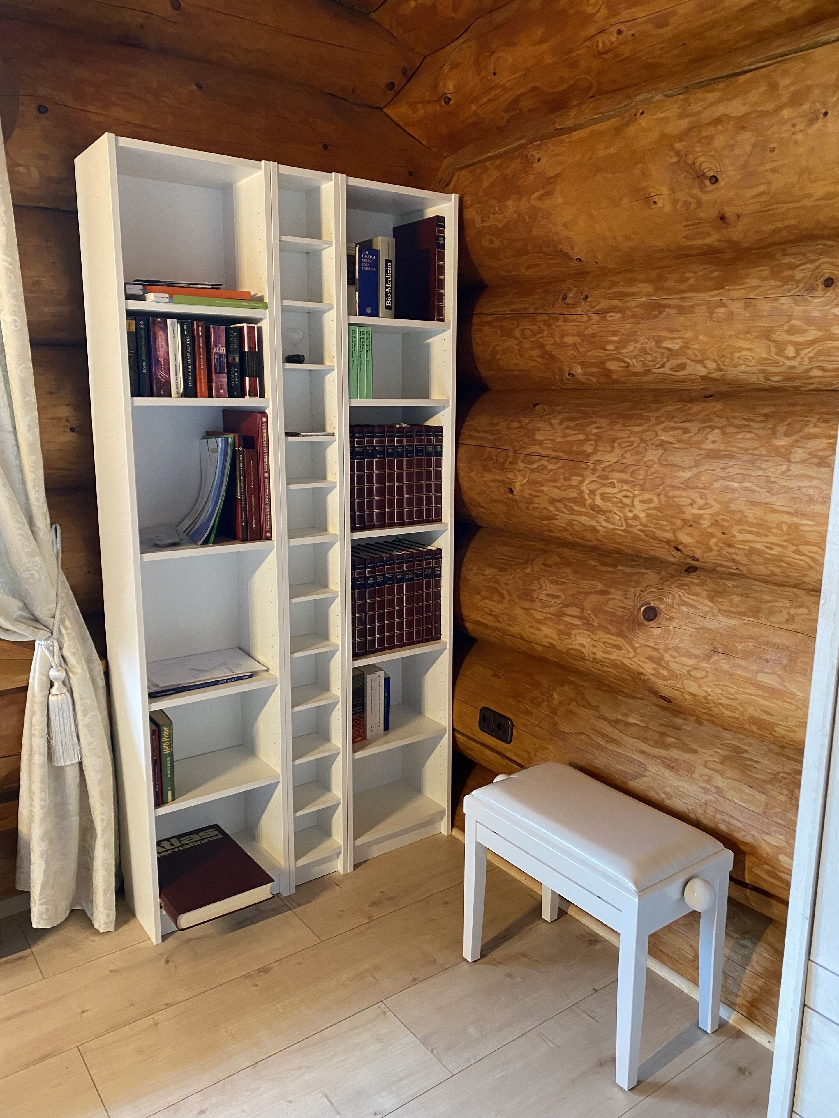 A white bookshelf against a wooden wall, with a small white bench beside it.