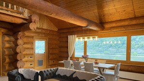 Ein rustikales Blockhaus-Interieur mit einer gemütlichen Sitzecke, einem Esstisch mit Stühlen und großen Fenstern mit Seeblick.