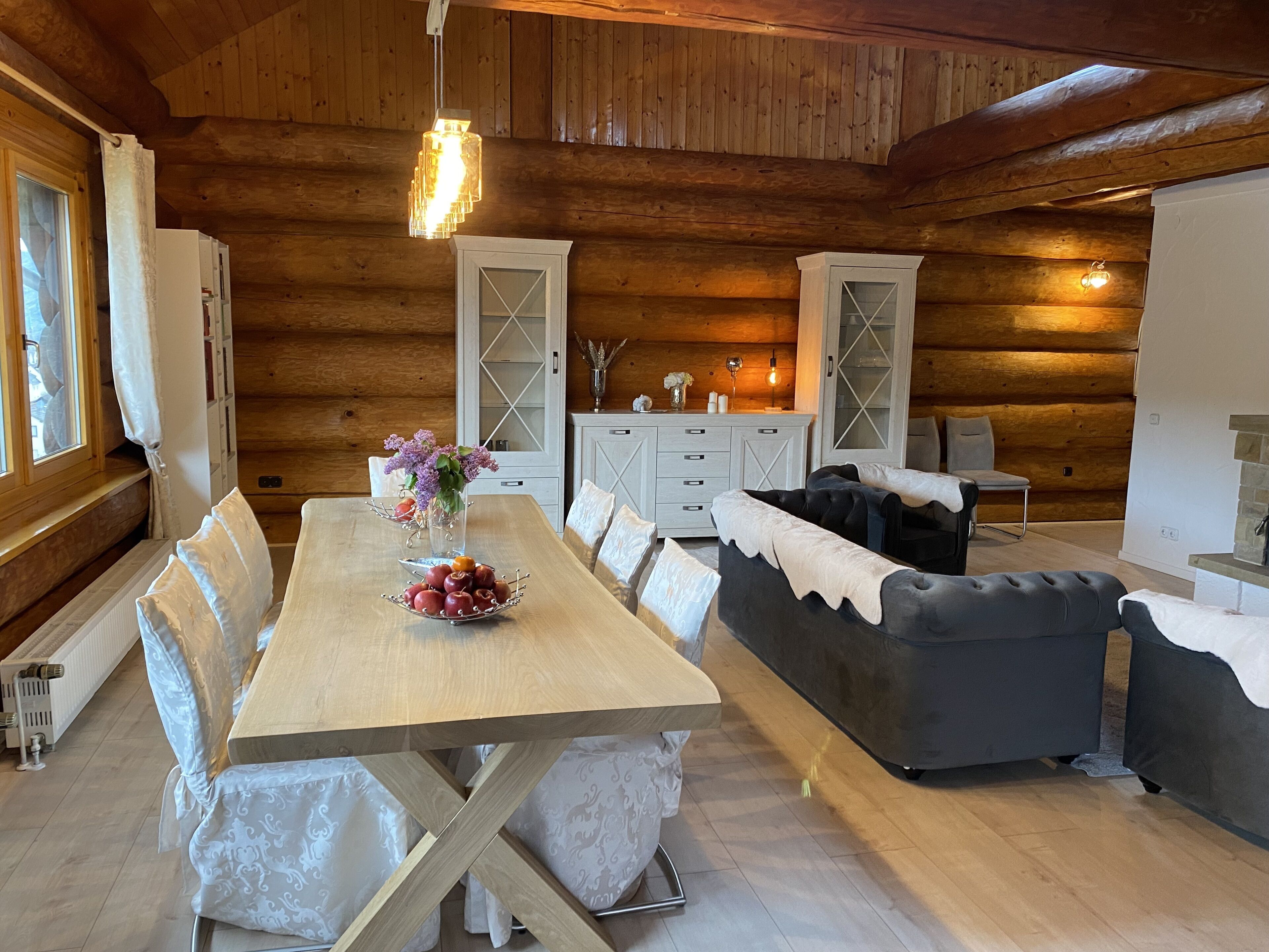Ein gemütliches Holzhäuschen mit Esstisch, Stühlen, einer Couch und einem Kamin.