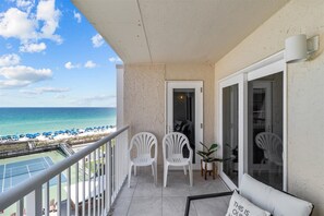 A balcony with a view of the beach and ocean, featuring two white plastic chairs and a small table with a cushion. - 611- Beautiful Newly Redecorated Unit with Gorgeous Gulf Views! (Destin)