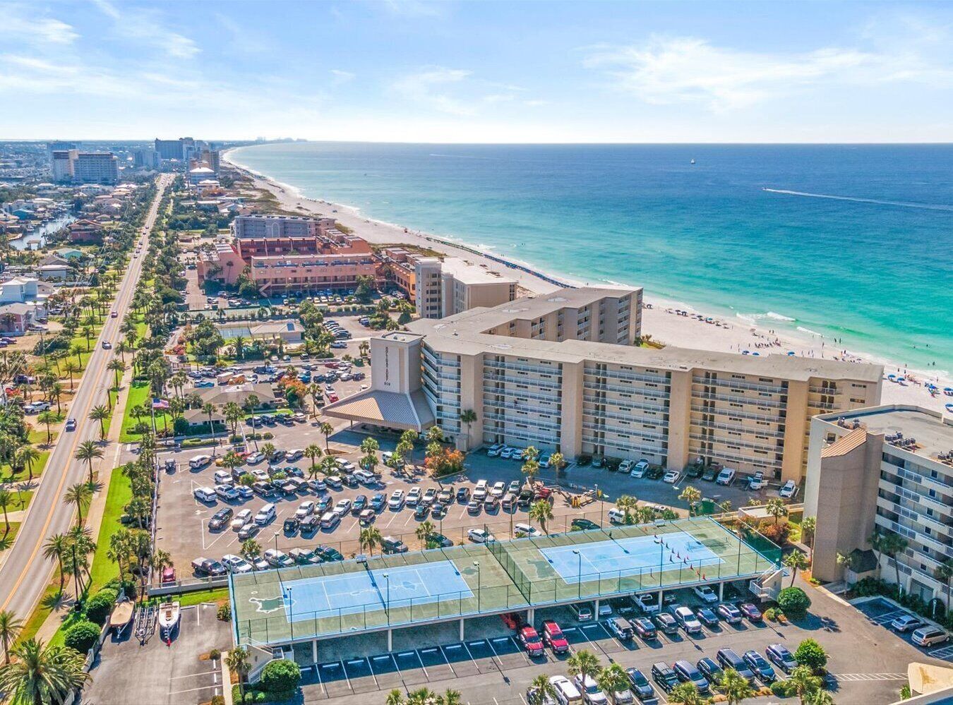 A coastal hotel with a parking lot, beachfront view, and a large building with multiple floors.