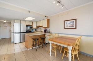 Una cocina compacta con una isla central, una mesa de comedor con sillas y un cuadro en la pared.