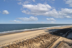A beach with a sandy shore, a wooden fence, and a clear sky with clouds.
