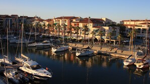 Un puerto deportivo con varias embarcaciones amarradas, rodeado de edificios de varios pisos con balcones y palmeras.