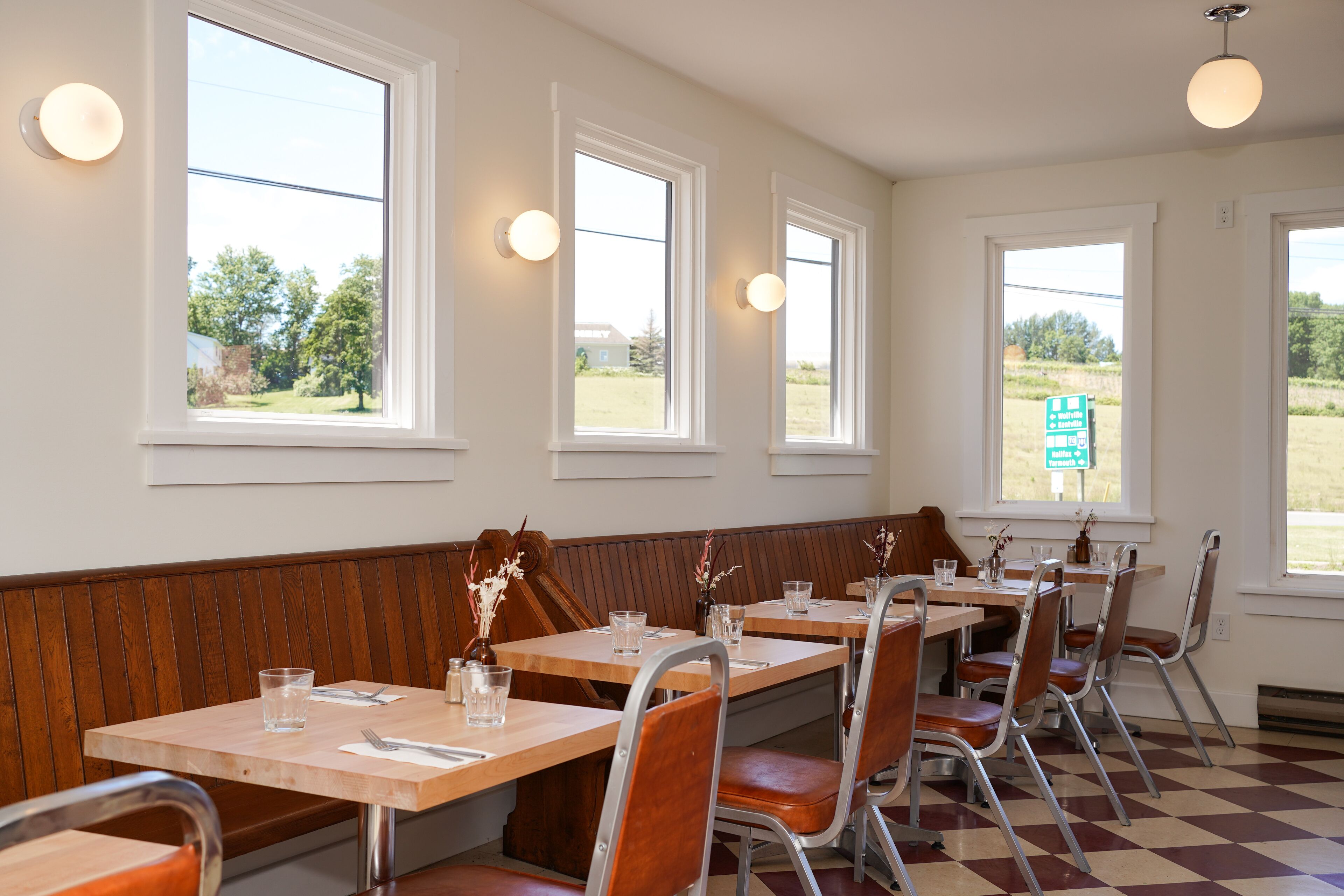 Un restaurant amb seients de fusta i taules, grans finestres amb vistes a la vegetació, i un patró de terra de taules de bàscula.