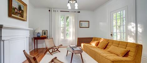 Una habitación con chimenea blanca, sofá amarillo, sillón de mimbre y mesa de centro de madera.