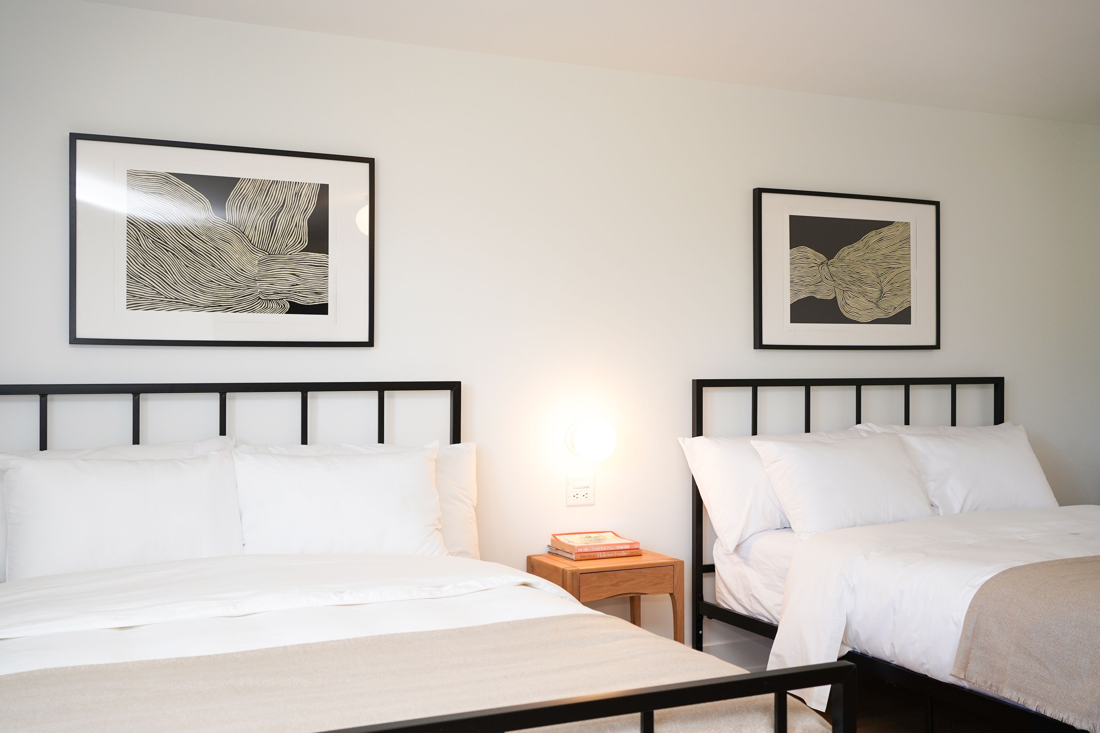Une chambre d’hôtel avec deux lits, une table de chevet avec une lampe et deux œuvres d’art encadrées au mur.