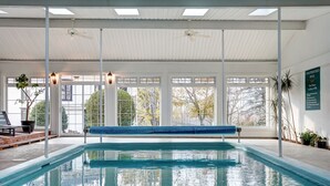 A swimming pool with a bench, large windows, ceiling fans, and a sign about pool hours. - The Evangeline (Grand Pre)