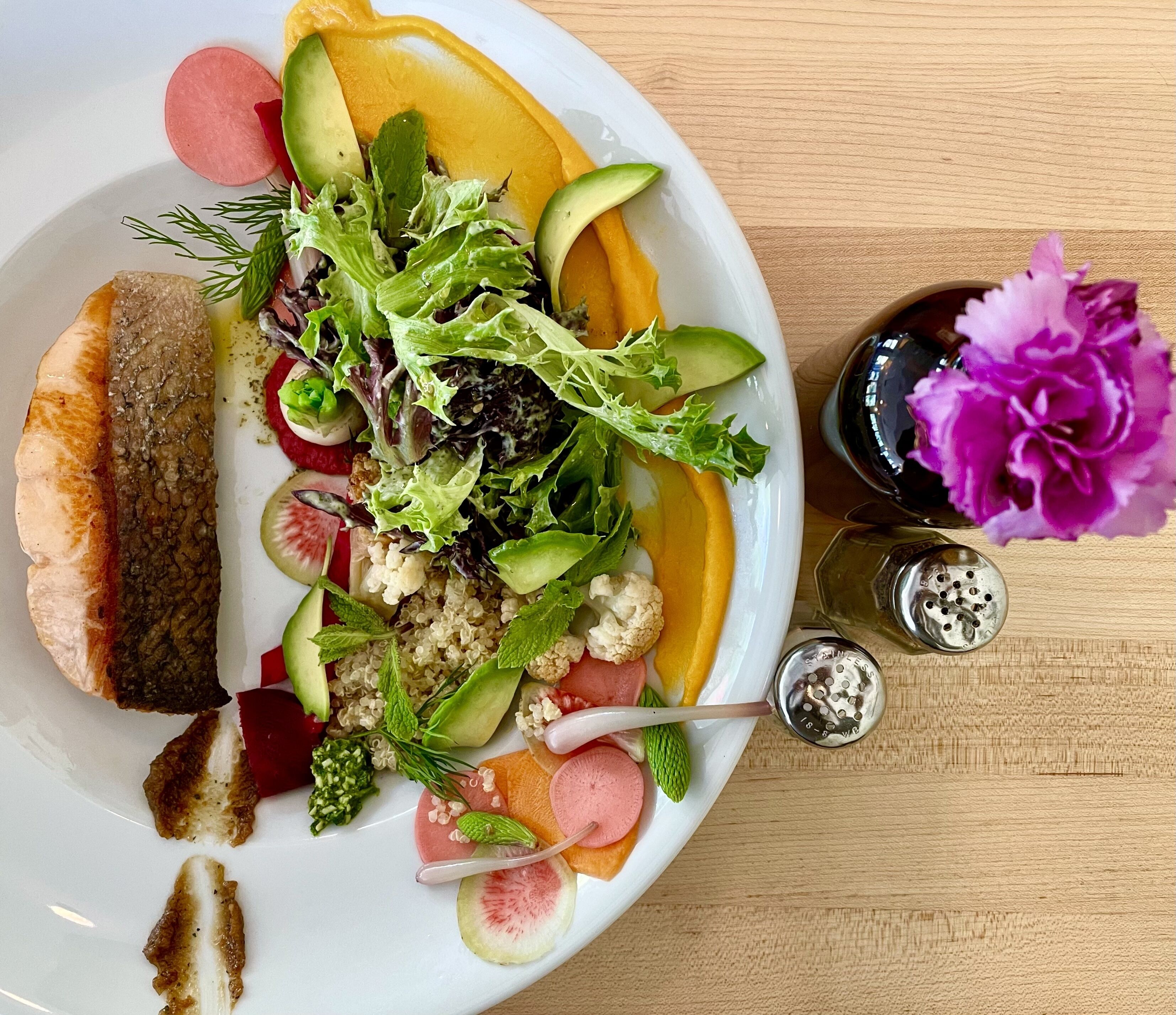 A plate with a variety of foods including fish, avocado, and salad.