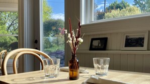 A dining table with two glasses and a vase of dried flowers, set against a window with a view of greenery. - The Evangeline (Grand Pre)