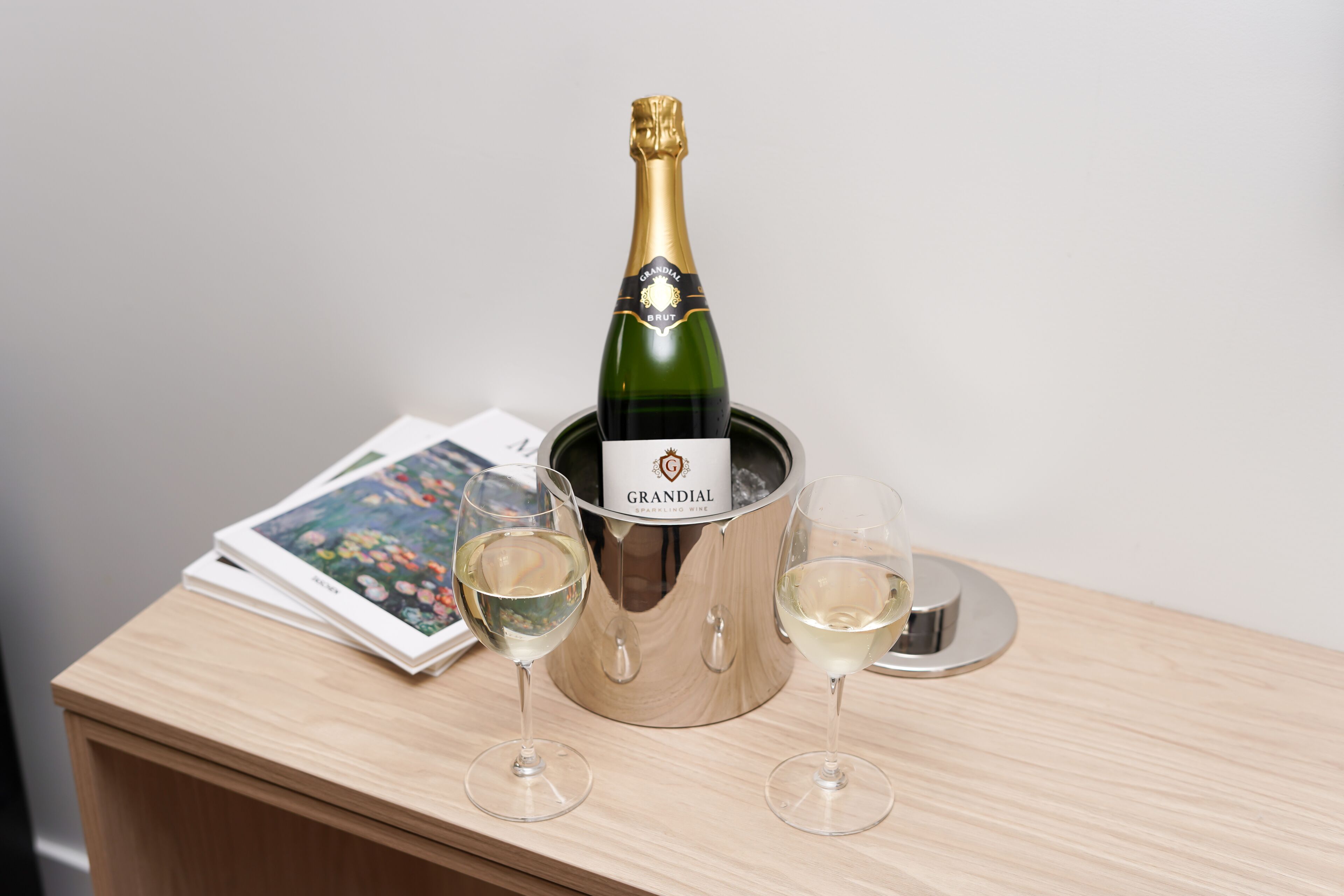 Une bouteille de vin mousseux Grandial dans un seau en métal, accompagnée de deux verres à vin posés sur une table en bois.