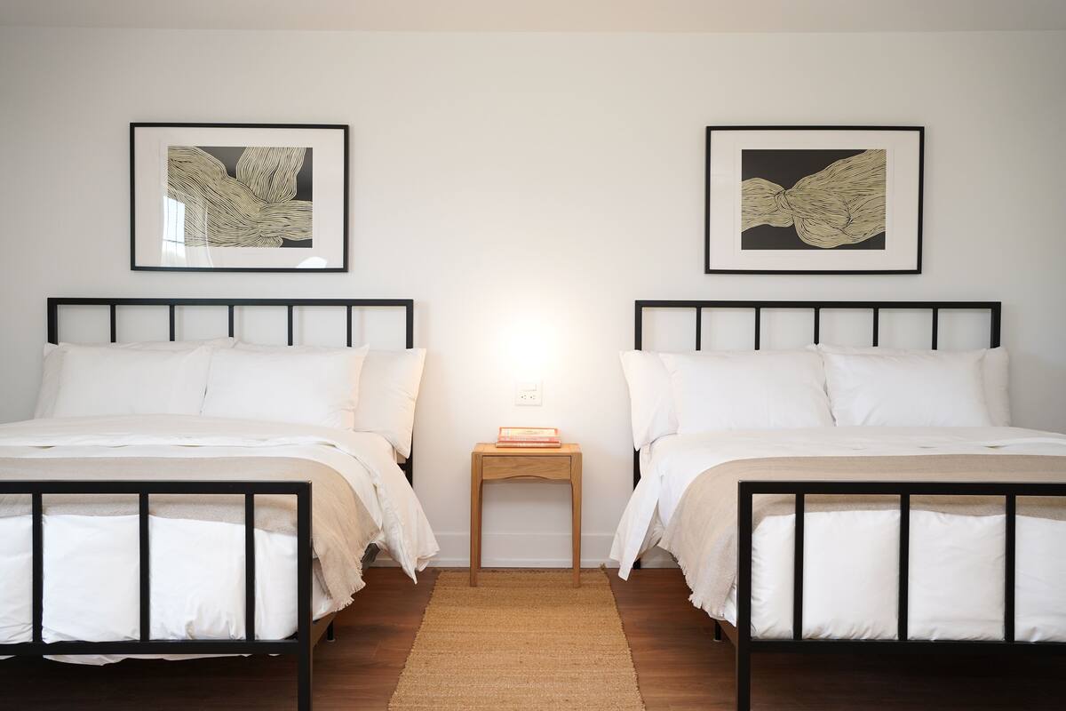 A room with two beds, a nightstand, and two framed artworks on the wall.