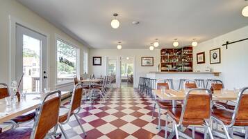 Un espace repas avec un sol à carreaux, des chaises et des tables en métal. On y trouve également un bar avec des étagères remplies de bouteilles et des tableaux encadrés accrochés au mur.