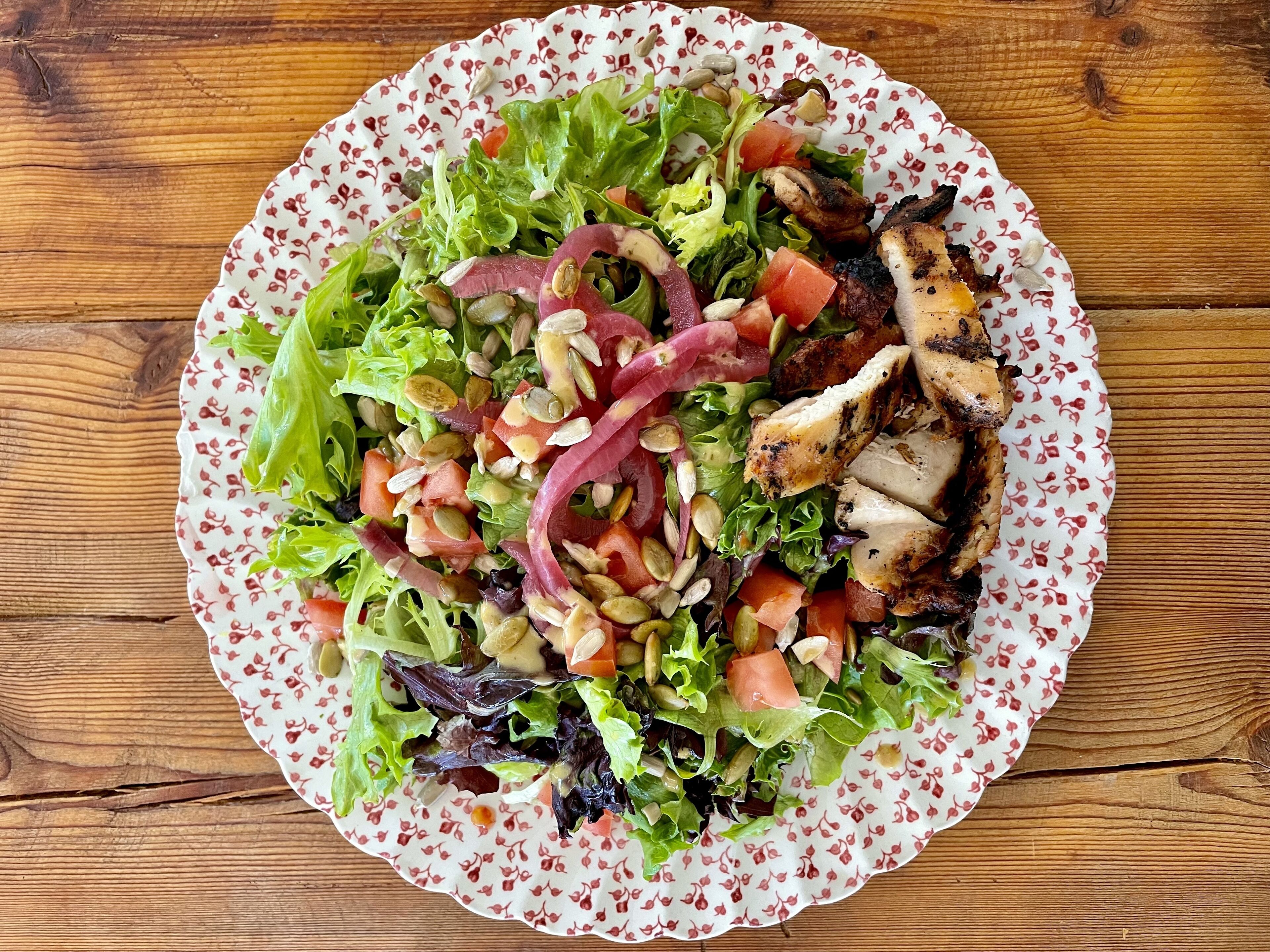 A plate of mixed greens salad with grilled chicken and nuts on a wooden table.