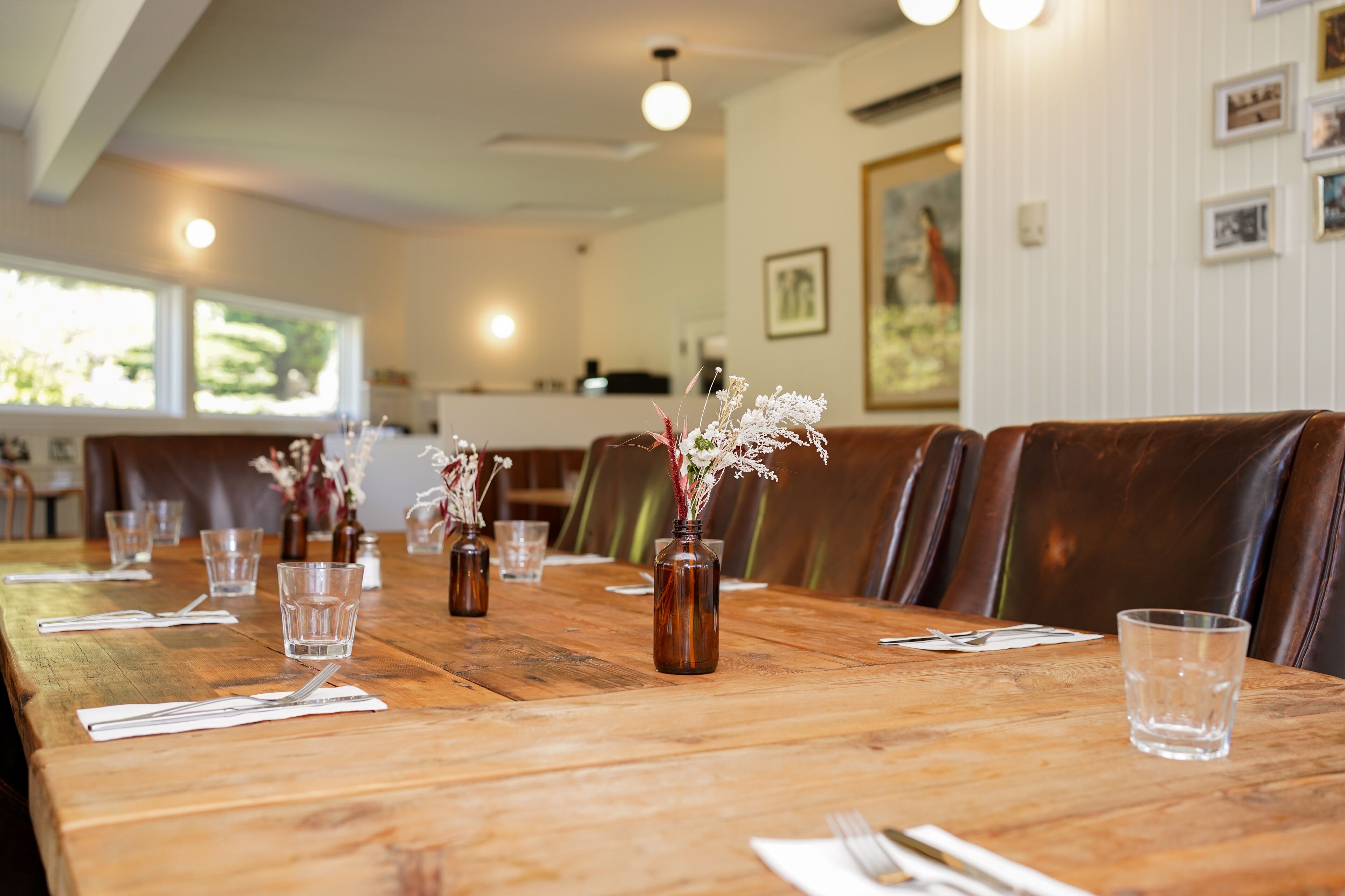 A long wooden dining table with vases of flowers, clear glasses, and neatly arranged cutlery.