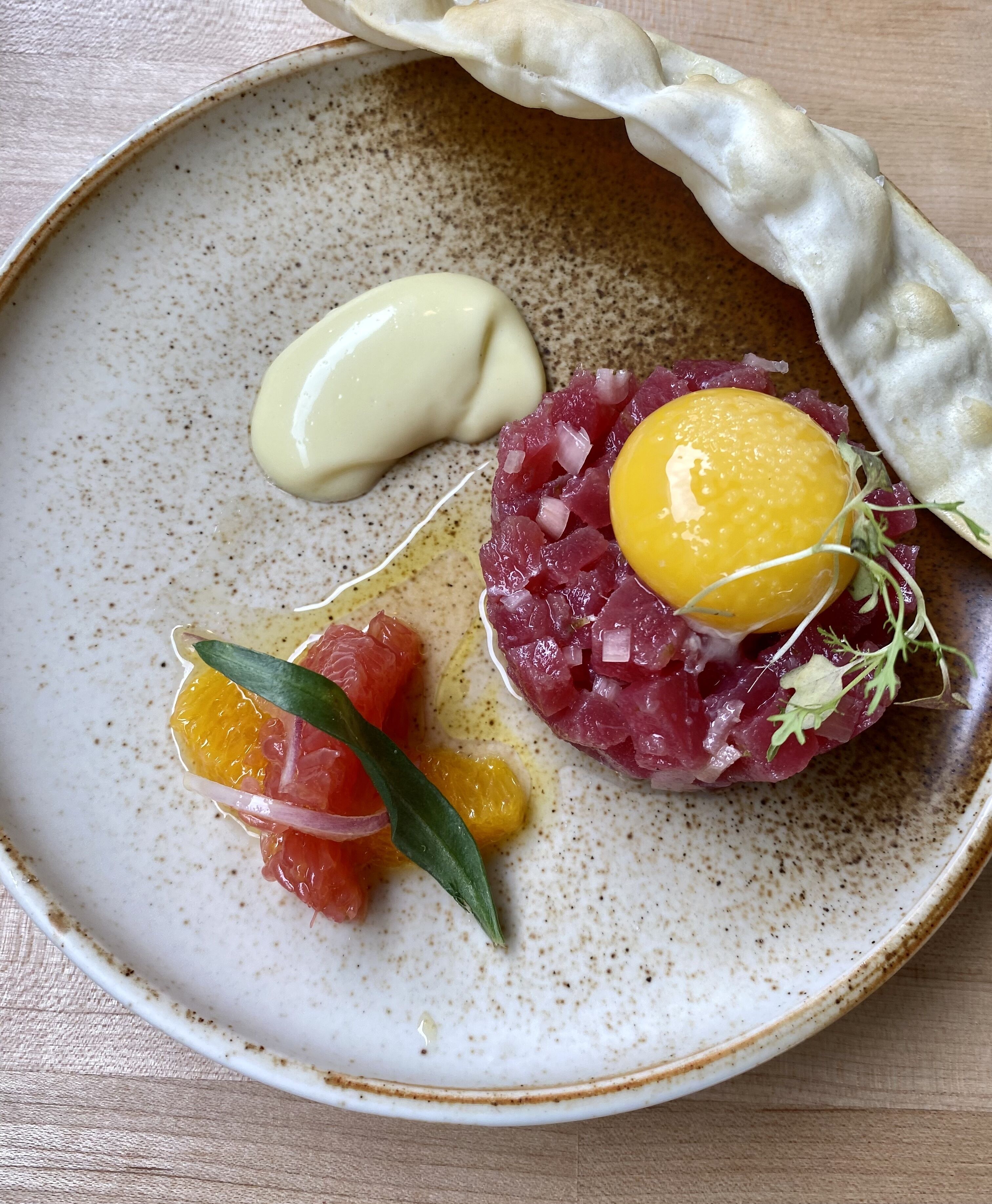Une assiette contenant un plat de poisson cru, un œuf et quelques agrumes.