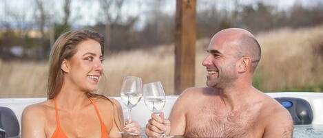 A couple in a hot tub with a wooden pergola overhead.