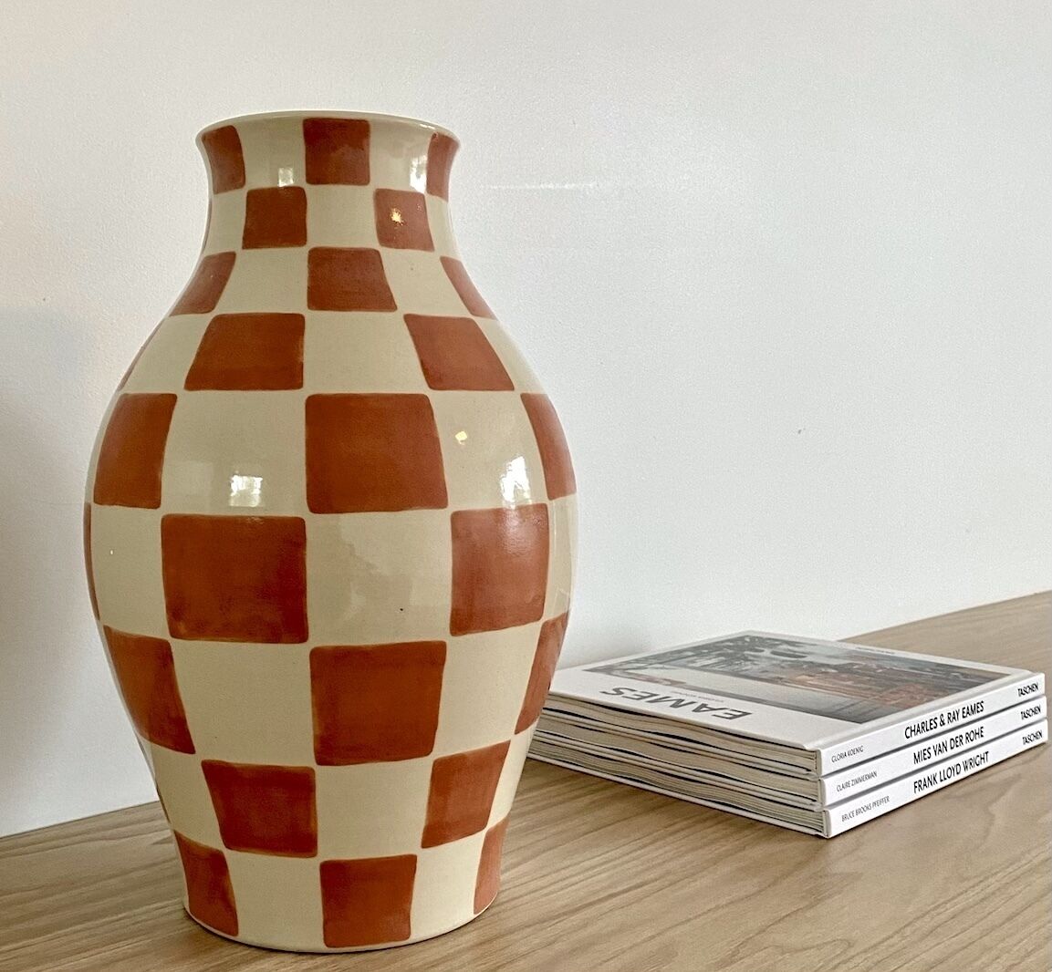 En keramisk vase med tern, placeret på en træoverflade ved siden af en stak blade.