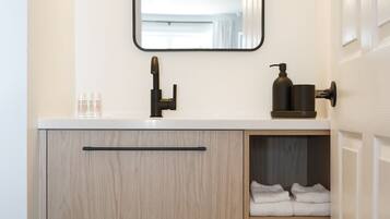 A modern bathroom with a white countertop, a black faucet, a mirror, and a wooden cabinet with towels.