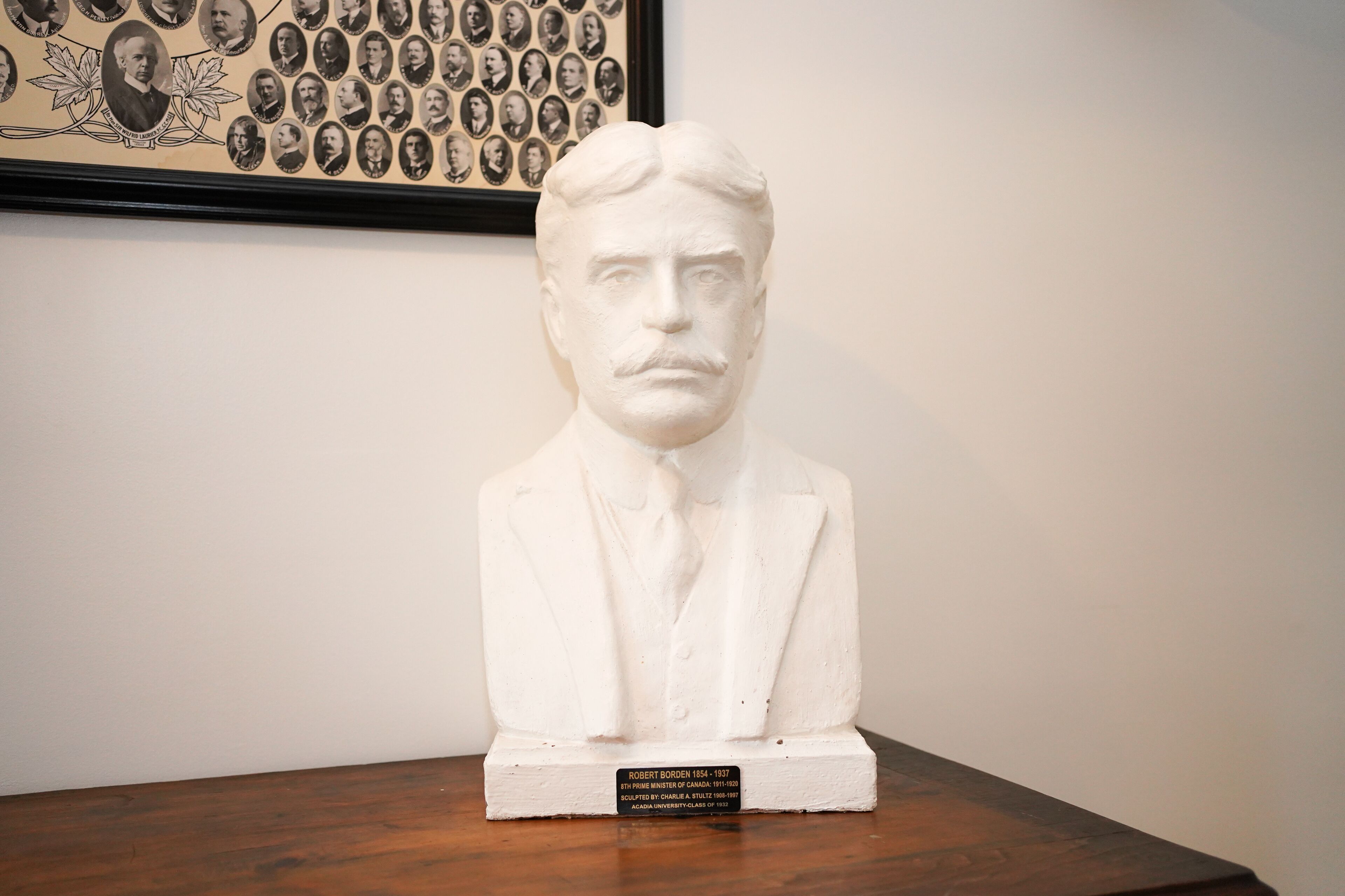 Une sculpture en buste, posée sur un socle en bois et agrémentée d’une plaque.